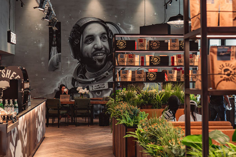 Space-themed wall mural and coffee setup at Black Sheep Coffee with lush greenery