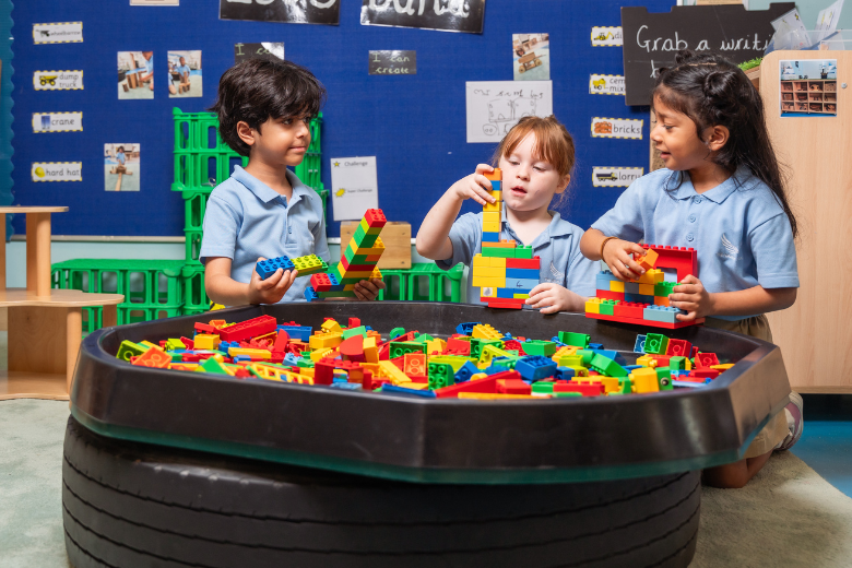 Children building with colourful Lego blocks in a creative learning space at The Aquila School EYFS.