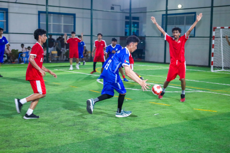 Students in red and blue jerseys compete during a fast-paced handball match at The Royal Academy Ajman.