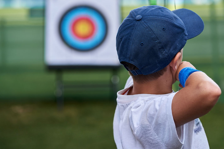 Child aiming at a target during archery lessons at Al Ain Adventure summer camp