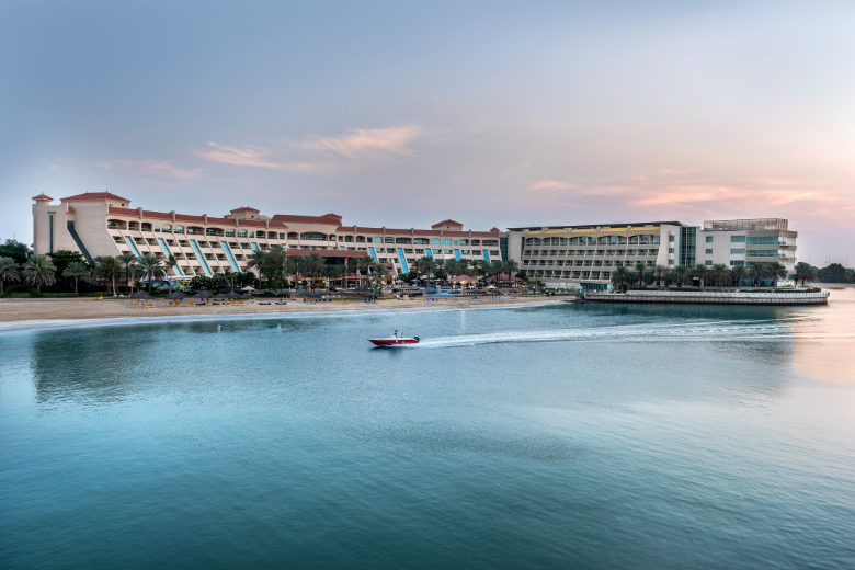 Scenic beachfront view of Al Raha Beach Hotel in Abu Dhabi at sunset with a speedboat on the water