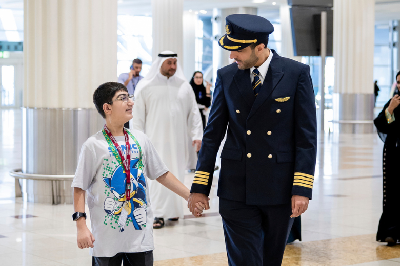 A Dubai airport pilot walks hand in hand with a smiling child of determination during an inclusive airport travel simulation.