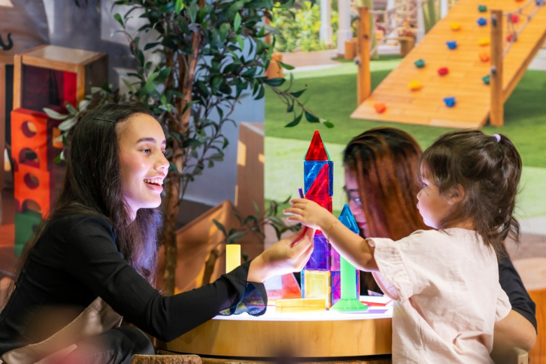 Teacher and child building colourful towers during a creative learning session at a Kids First Group nursery.