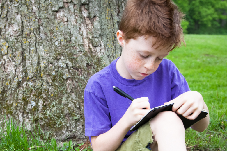 Young student journaling outdoors as part of mindfulness and wellbeing practices in education.