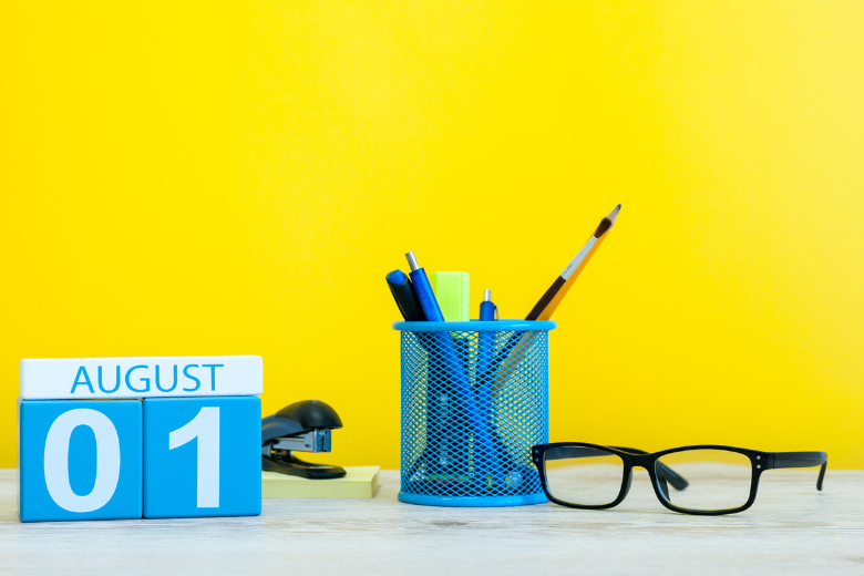 Desk calendar showing August 1 with school supplies on a bright yellow background