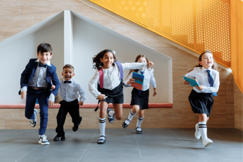 Happy schoolchildren in uniform running through a modern school hallway