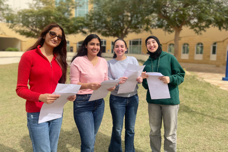 Four Brighton College Abu Dhabi students smiling and holding A-Level results envelopes