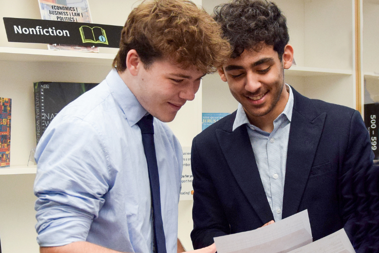 Two Brighton College Dubai students smiling while looking at their A-Level results in the school library