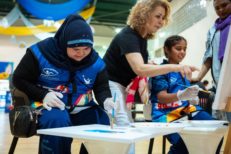 A student of determination painting with guidance from a teacher during KHDA summer programme activities.