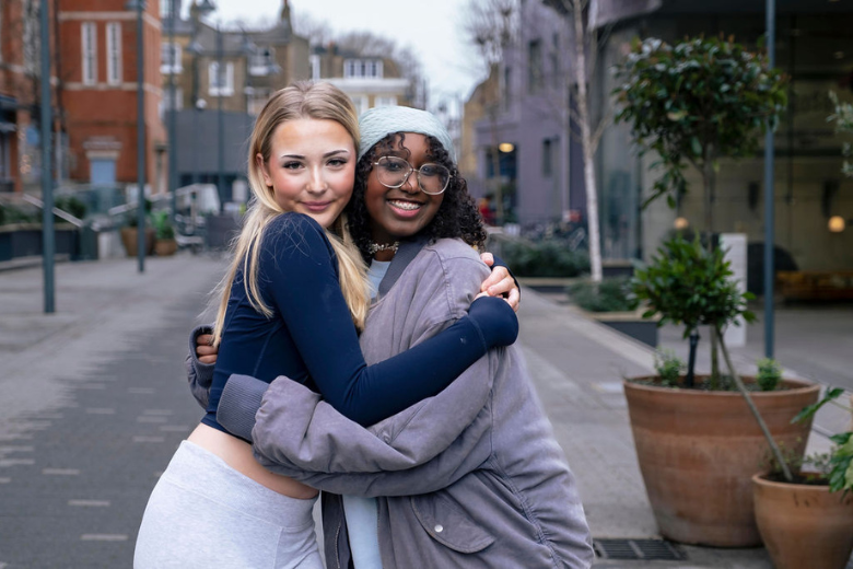 Two Minerva Virtual Academy students hugging and smiling in a UK street scene.