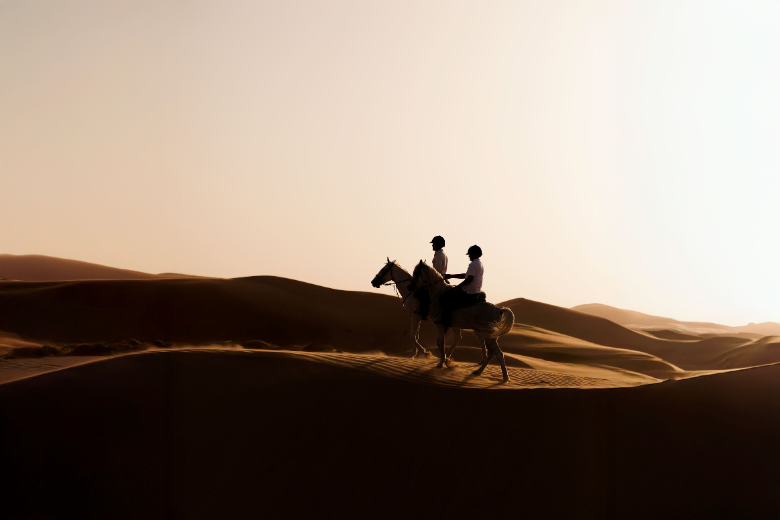 Guests horseback riding across the rolling dunes of the Liwa Desert at Qasr Al Sarab.