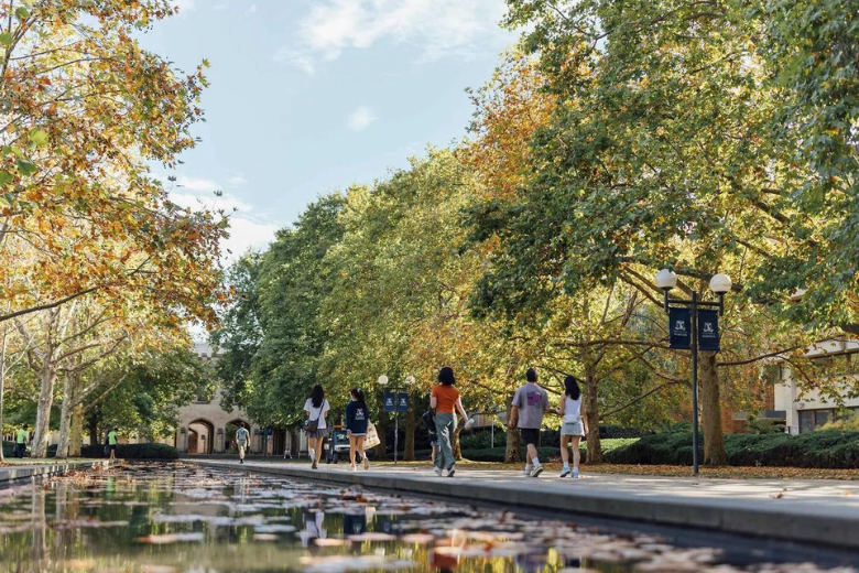 Students walking along the University of Melbourne campus surrounded by autumn trees