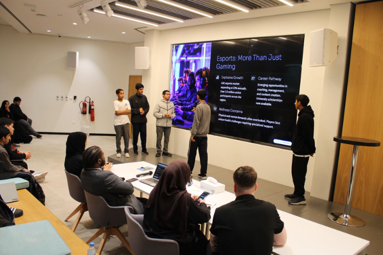 Students present an esports project to peers in a modern learning space with a large screen