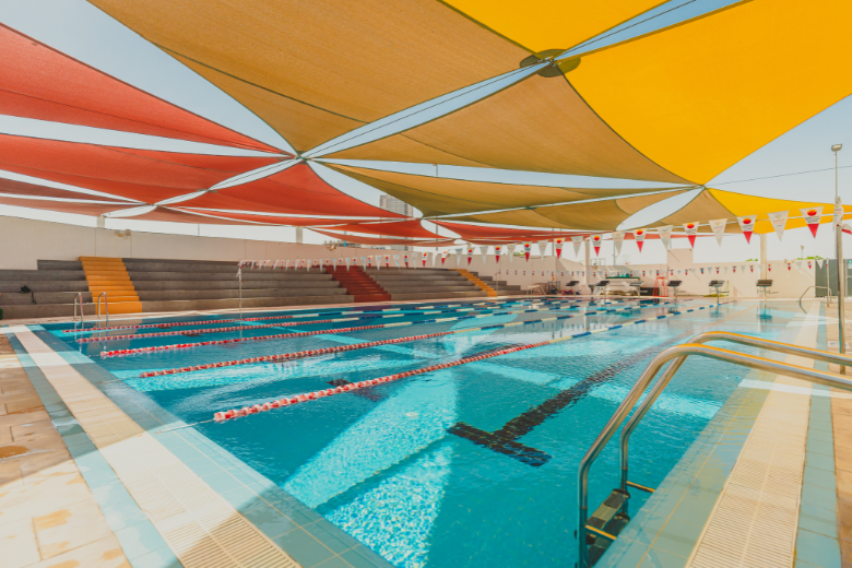 Outdoor swimming pool at Dunecrest American School with shaded seating and bright canopies